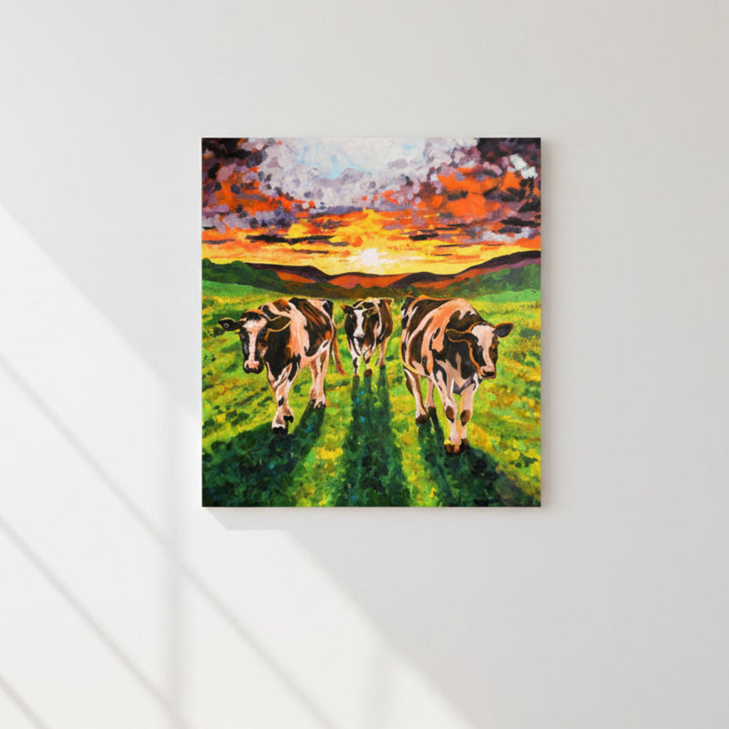 Painting of three cows in a field with a colorful sunset on a white wall.